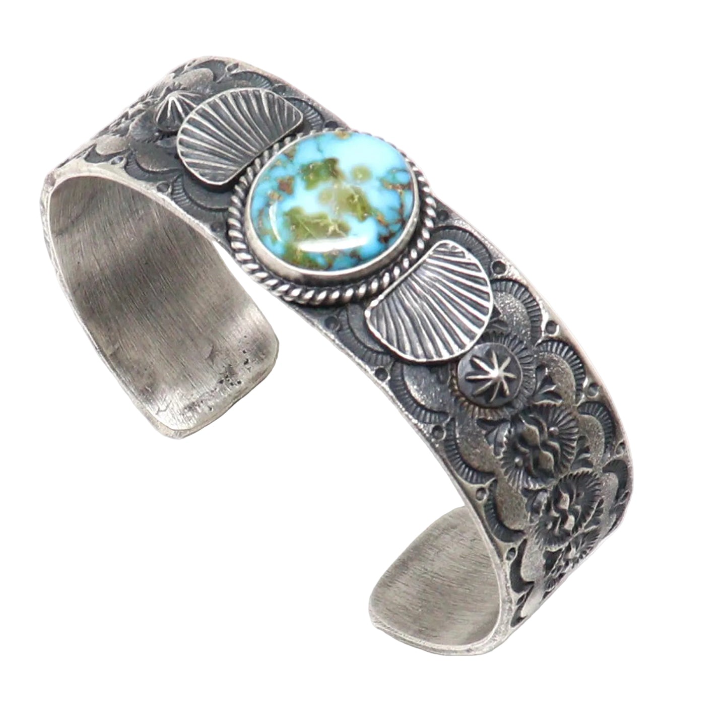 A silver cuff bracelet featuring a central oval turquoise cabochon with green matrix, surrounded by detailed floral and shell-like engravings on a white background.
