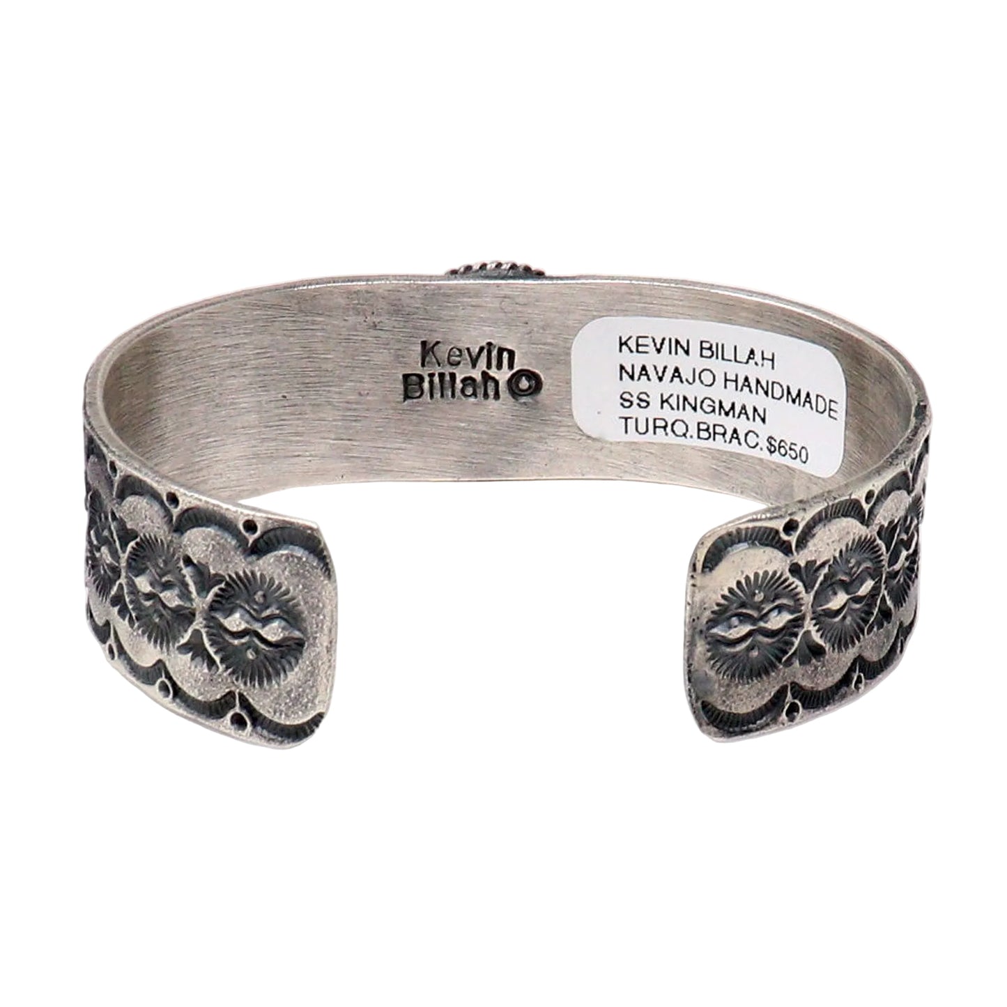 A silver open cuff bracelet with dark oxidized floral and geometric engravings on both ends, photographed on a white background. The inside of the cuff is stamped with 'Kevin Billah' and a white product label is attached.