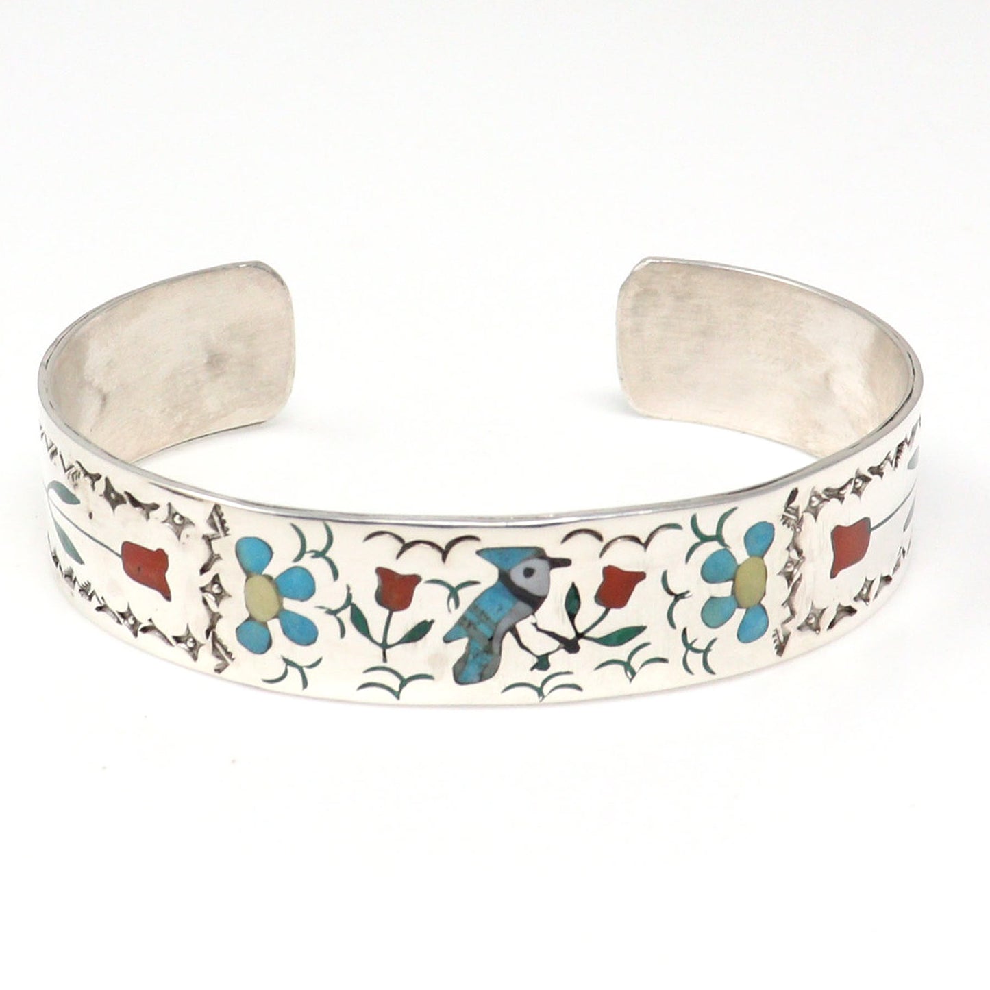 A silver cuff bracelet featuring colorful inlay details of flowers, leaves, and a bluebird on a white background.