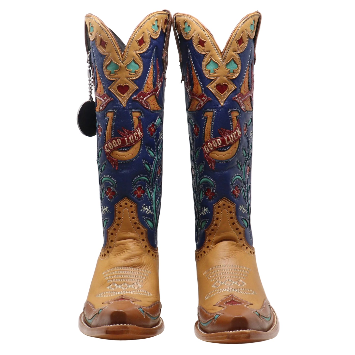 A pair of cowboy boots with tan leather lower sections and blue shafts decorated with embroidered floral patterns, turquoise accents, and a large embroidered horseshoe design with the words 'GOOD LUCK'.