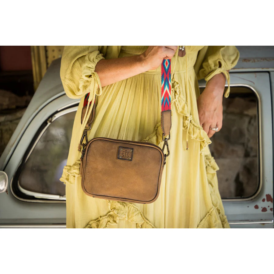Person wearing a yellow dress holding a brown leather crossbody bag with a colorful strap.