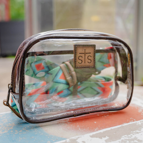 Clear cosmetic bag with brown handle and visible brand logo on a colorful surface.