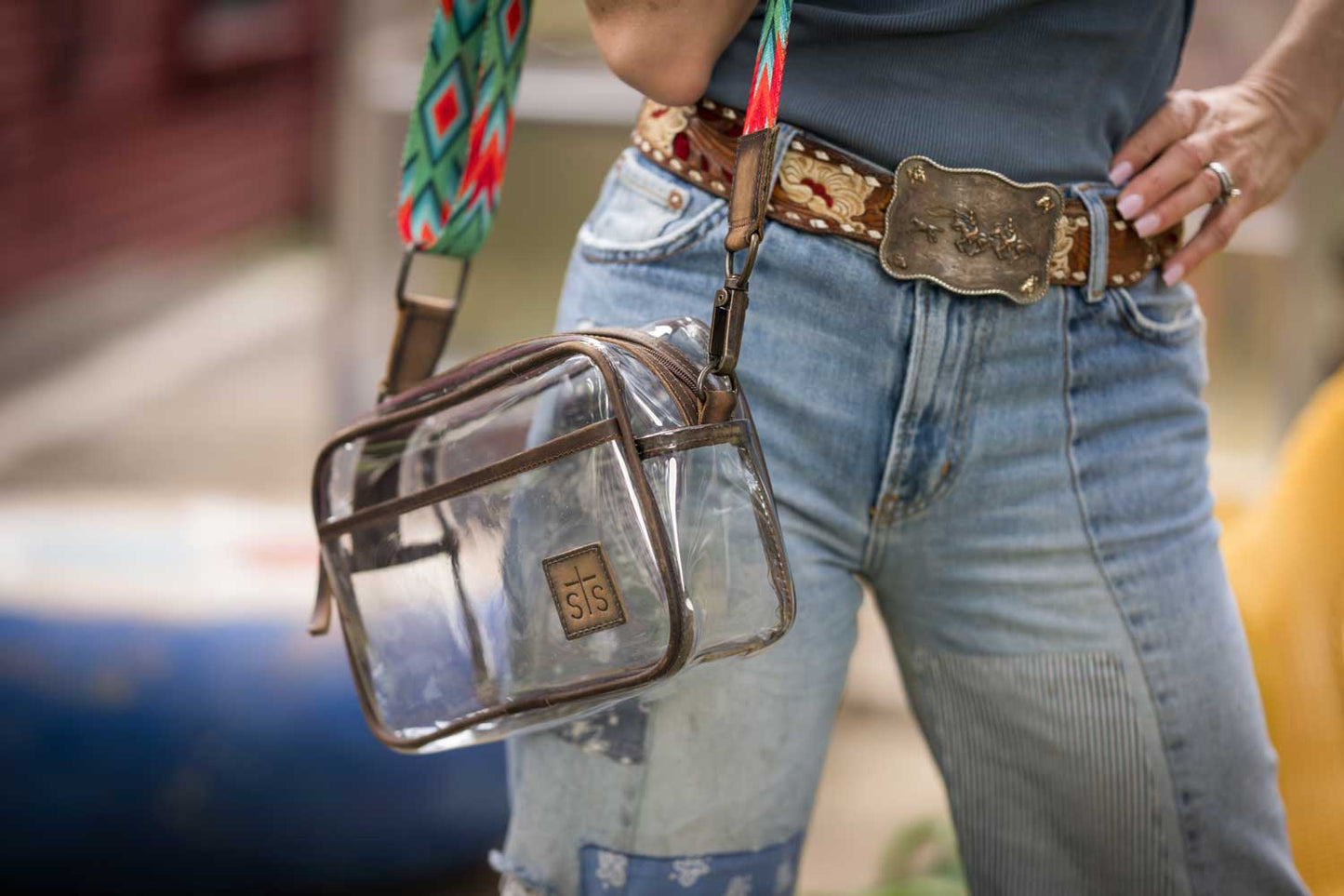 Person wearing a transparent handbag with a colorful strap and denim jeans.