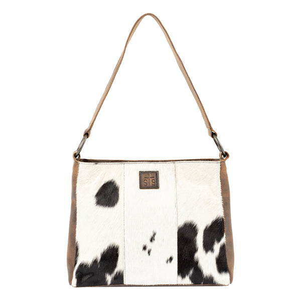 A shoulder bag featuring a cowhide pattern with black and white patches, tan leather trim, and a matching tan shoulder strap. A small brown leather logo patch with 'S16' is visible on the front.