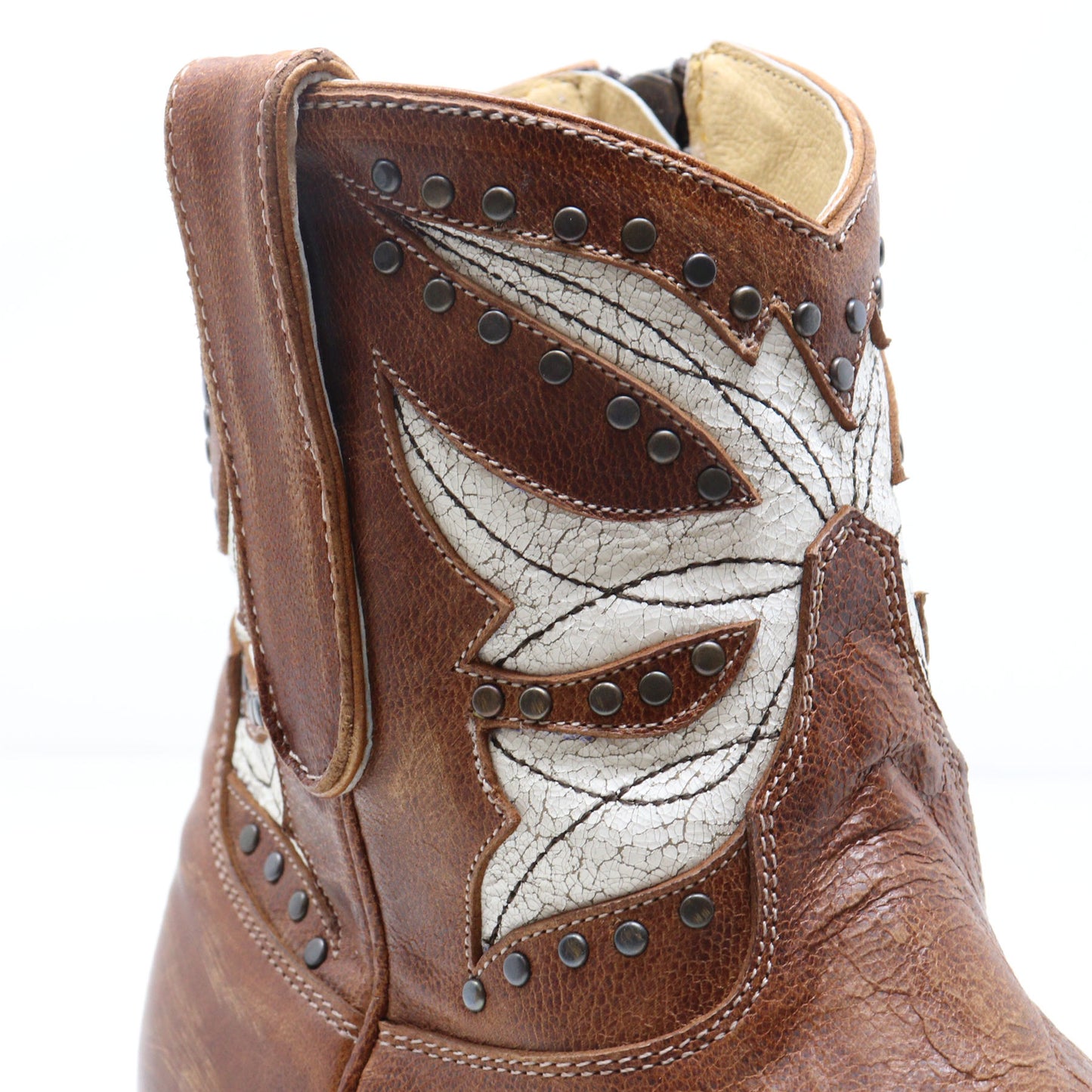 A close-up of a brown leather western boot featuring a large white cracked-leather wing applique with dark metal studs on a white background.