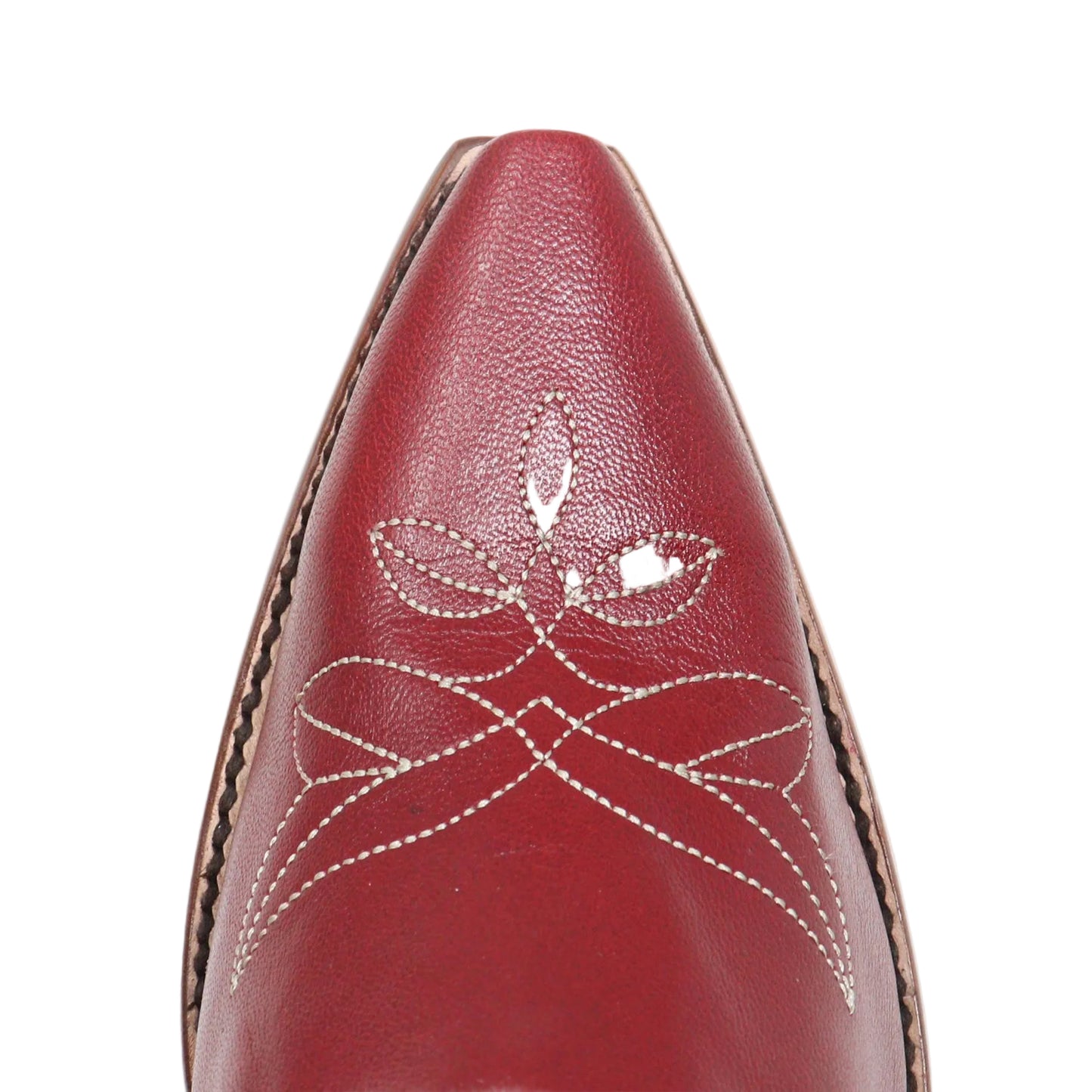 A close-up of a red leather pointed shoe toe with decorative white stitching and contrast brown stitching along the side, shown against a plain white background.