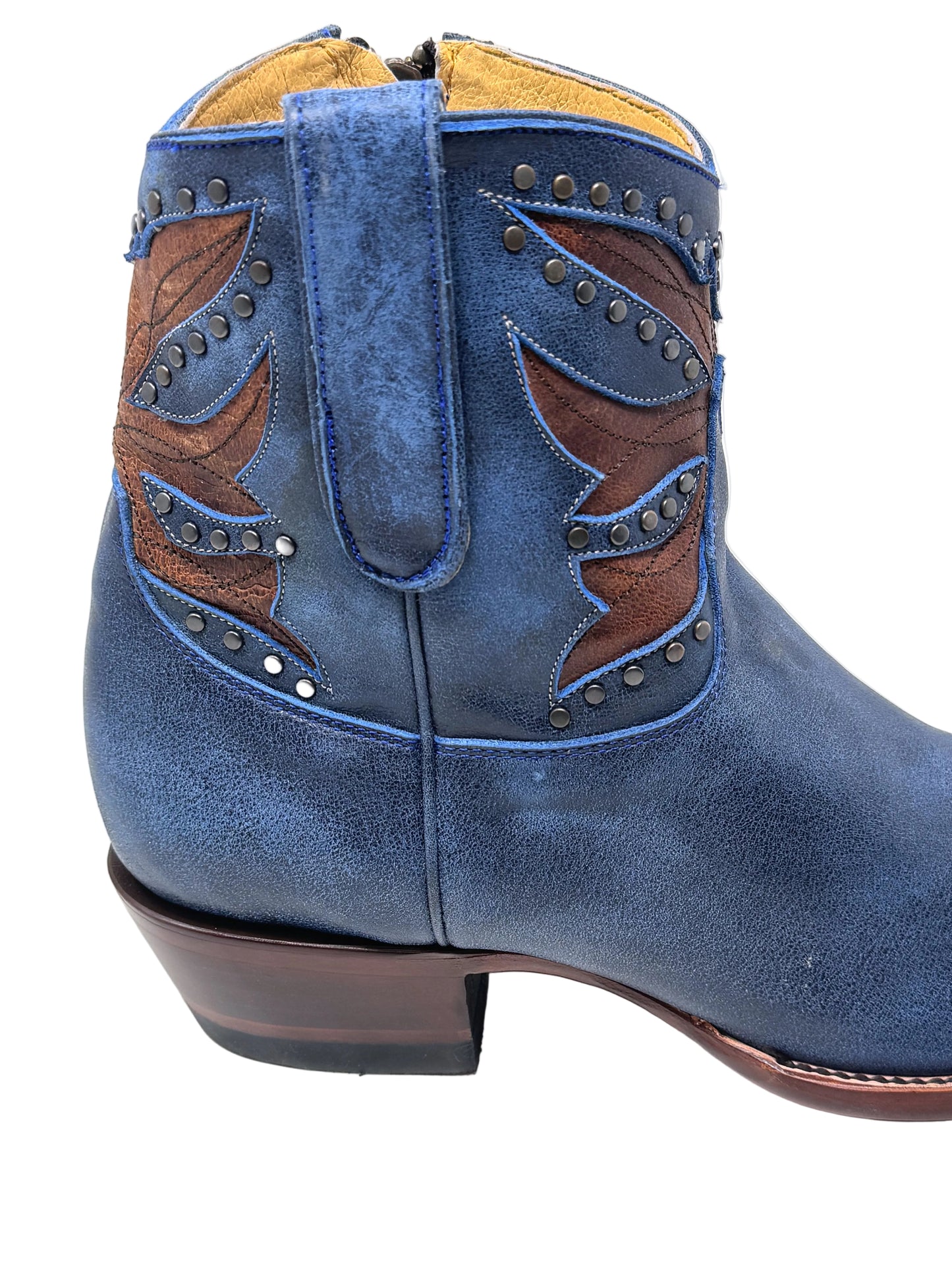 A close-up side view of a blue suede western boot with brown leather wing-shaped embroidery, silver studs, and a dark brown stacked heel on a white background.